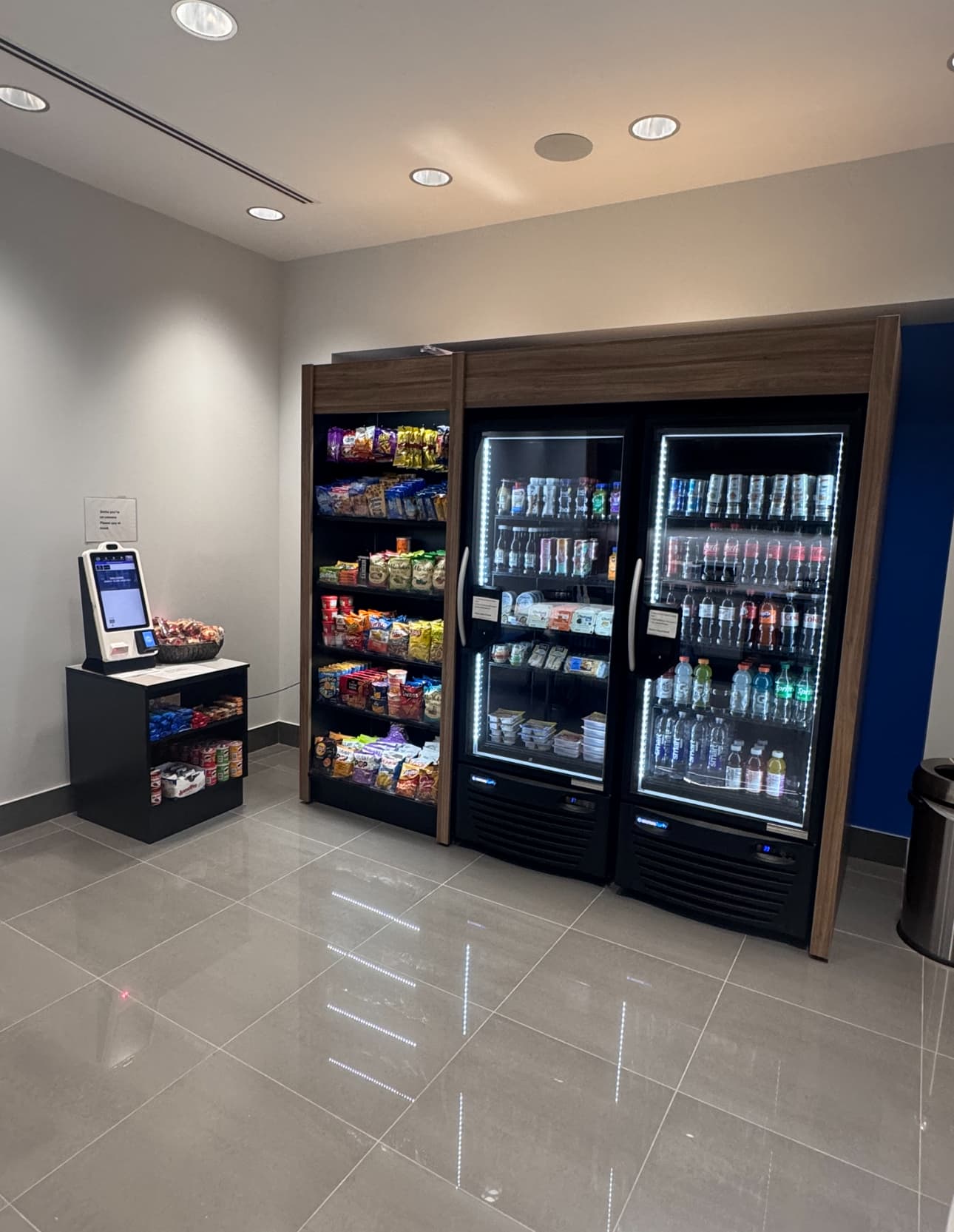 Apartment lobby micro market with a kiosk, snack shelves and glass-door coolers