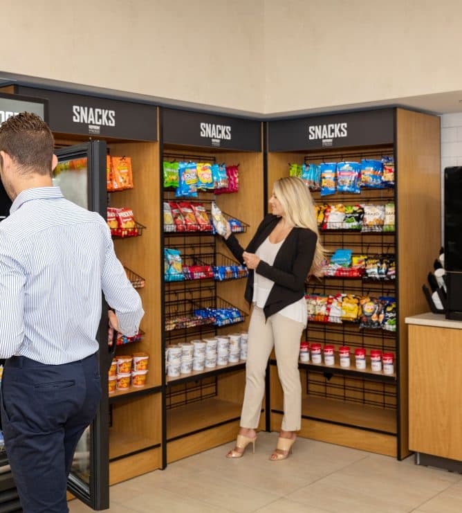 Two employees browsing the snack and cooler wall of an office micro market