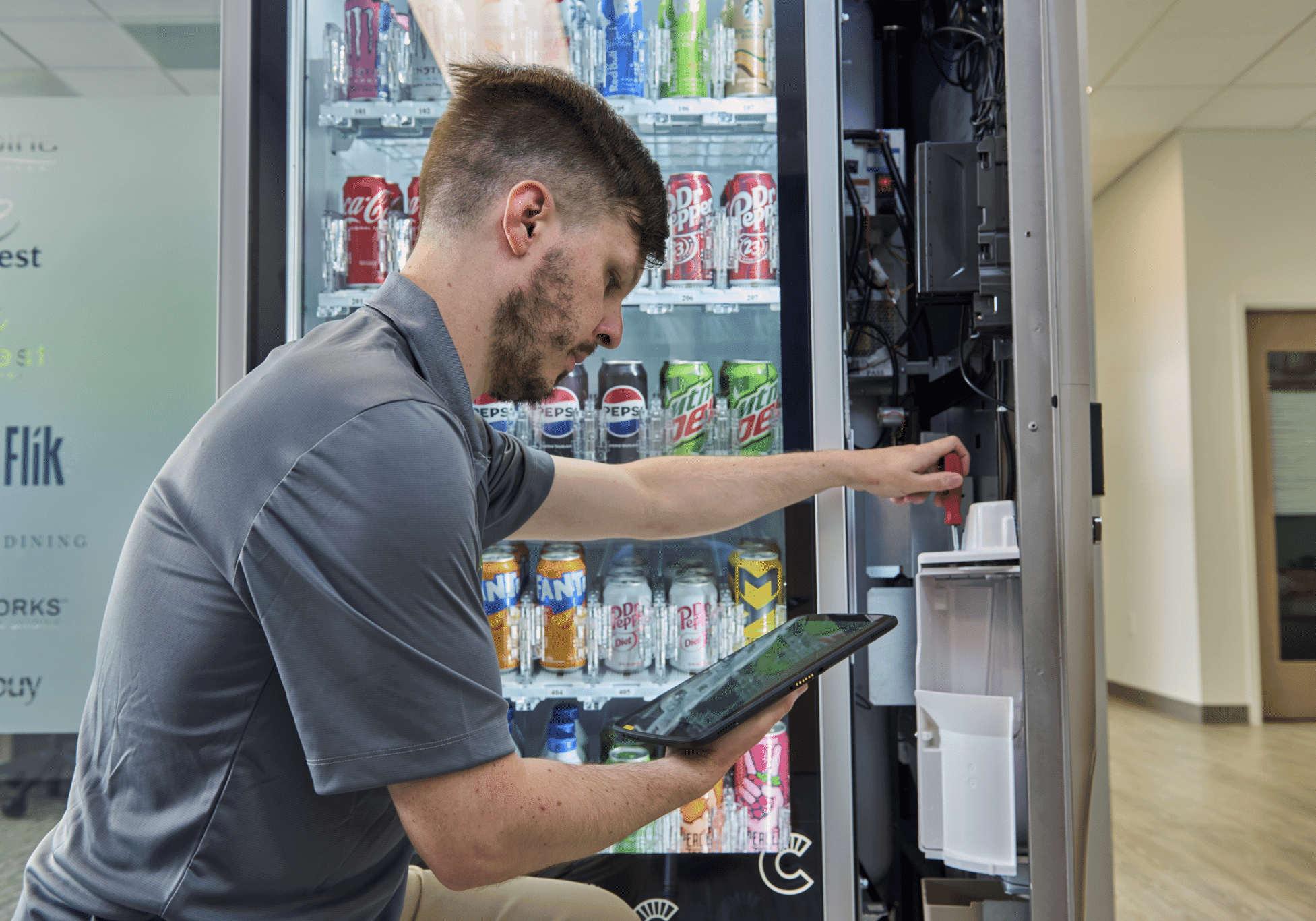 Automated Amenities technician restocking a vending machine while checking a tablet